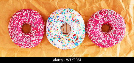 Tre ciambelle colorate su carta gialla borsa. Banner. Close up, vista dall'alto. Foto Stock