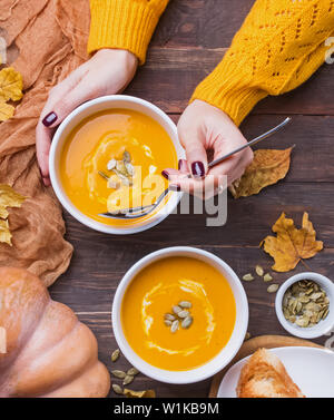Donna di mani tabella sppoon vicino la ciotola di delecious fatti in casa zuppa di zucca con crema di latte sul tavolo di legno vista superiore Foto Stock