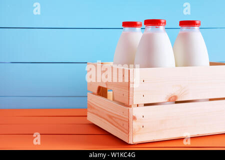 Tradizionali bottiglie di latte in una cassa di legno su orange paese in legno tavolo da cucina con blu sullo sfondo di legno. Foto Stock