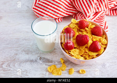 Un bicchiere di latte e una ciotola di cereali secchi fiocchi di mais con topping di fragole su un tavolo di legno. Vista superiore Foto Stock