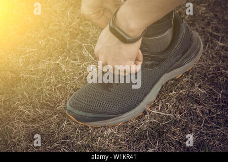 Un giovane uomo vestiti di nero è la legatura i lacci sul sneakers vicino atleta fitness seduta sul campo sportivo sull'erba. riscaldare corpo prepa Foto Stock