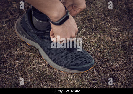 Un giovane uomo vestiti di nero è la legatura i lacci sul sneakers vicino atleta fitness seduta sul campo sportivo sull'erba. riscaldare corpo prepa Foto Stock