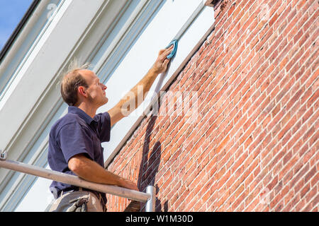 Pittore europeo sui ponteggi pulizia di stampaggio del tetto con un panno Foto Stock