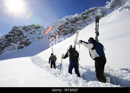 Per la ricerca di untracked polvere di neve. Tre uomini a portare i loro sci su uno zaino su un pendio di neve. Lech, Zürs, Zuers, Arlberg, Oesterreich, Austria, un Foto Stock