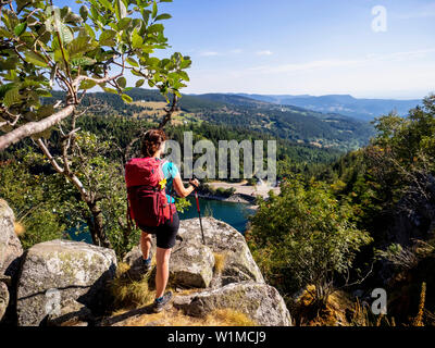 Vista posteriore delle donne escursionista cercando in vista della foresta da Hans roccia sopra bordo Lac Blanc al Rocher Hans, Francia Foto Stock