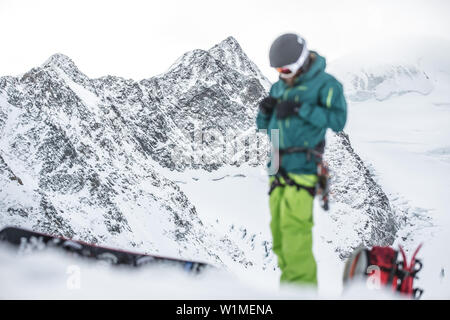 Giovane maschio snowboarder preparando le sue cose in montagna, Pitztal, Tirolo, Austria Foto Stock