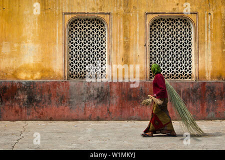 Donna con spazzole di bambù di fronte ad un edificio nel tempio Galtaji, Jaipur, Rajasthan, India Foto Stock