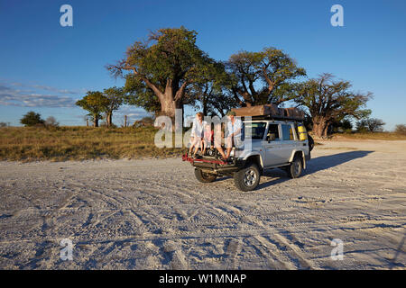 Famiglia seduta su un veicolo fuoristrada al tramonto, Tutume, Nxai Pan National Park, Botswana Foto Stock