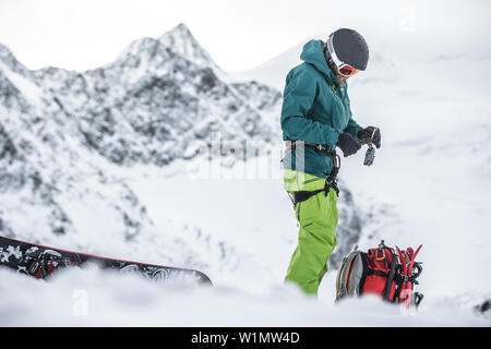 Giovane maschio snowboarder preparando le sue cose in montagna, Pitztal, Tirolo, Austria Foto Stock