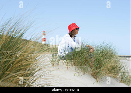 Donna che indossa una capanna rosso seduto alla spiaggia, List-Ost faro in background, Ellenbogen, elenco, Sylt, Schleswig-Holstein, Germania Foto Stock
