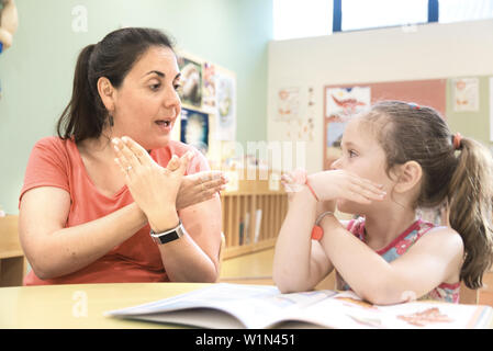 Insegnante di lingua dei segni in un tutoraggio extra di classe con un bambino sordo ragazza utilizzando American Sign Language. Foto Stock