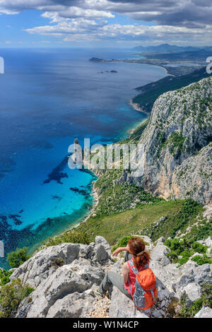 Donna escursionismo Selvaggio Blu seduta a Punta Giradili e guardando alla costa del Golfo di Orosei con guglie di roccia Pedra Longa, Selvaggio Blu, Parco Nazionale Foto Stock