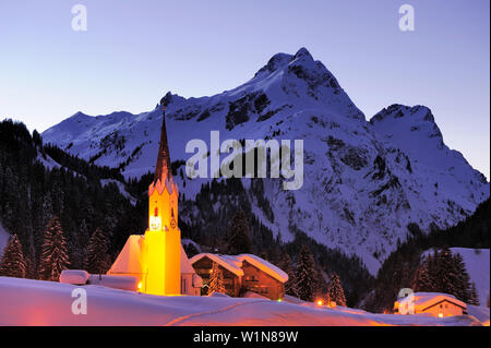 Chiesa illuminata nella parte anteriore del paesaggio di montagna, Schroecken, Vorarlberg, Austria Foto Stock