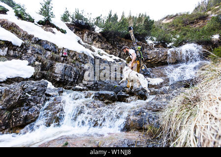 Backcountry rider e il suo cane che attraversa un ruscello in Ammergauer Alpi, Baviera, Germania Foto Stock