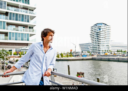 Metà uomo adulto appoggiata contro la balaustra, Marco-Polo-torre in background, HafenCity di Amburgo, Germania Foto Stock