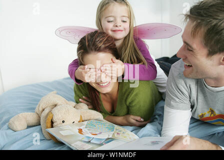 Famiglia giovane sdraiato sul letto mentre la lettura di un libro, Monaco di Baviera, Germania Foto Stock