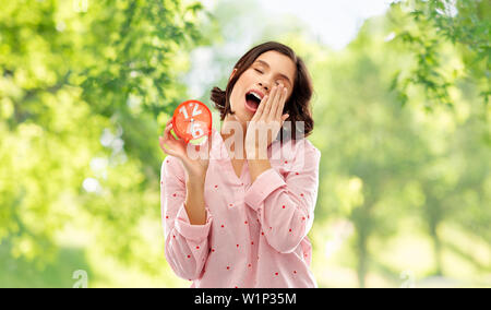 Assonnato donna in pigiama con sveglia sbadigli Foto Stock