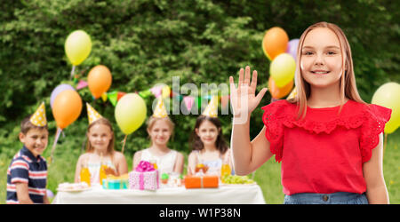 Ragazza sorridente agitando la mano alla festa di compleanno nel parco Foto Stock