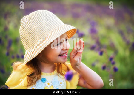 Carino sorridente bambina in beige hat all'aperto nel campo verde. Ritratti di bambini Foto Stock