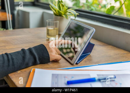 Vista dettagliata del dito indice toccando lo schermo tablet sul tavolo di legno Foto Stock