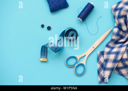 Accessori per il cucito con filettature, forbici, perni, tessuto, pulsanti e la cucitura di nastro su sfondo blu. Vista dall'alto. Lay piatto. Foto Stock