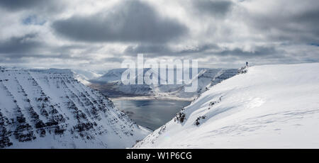 Alpinista di sci in piedi sulla cima di una montagna della tavola e si gode della vista sul fiordo del paesaggio, a ovest di fiordi, Islanda Foto Stock