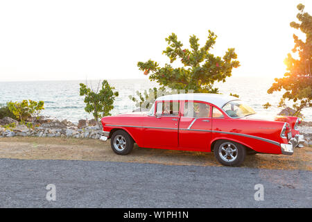 Oldtimer rosso su una solitaria strada costiera di La Boca di Playa Ancon, con belle piccole spiagge tra mare blu turchese, famiglia viaggi a Cuba, p Foto Stock