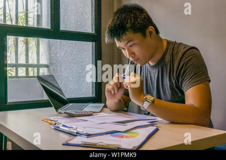 Giovane maschio asiatici freelancer lavorando su laptop e documenti Foto Stock
