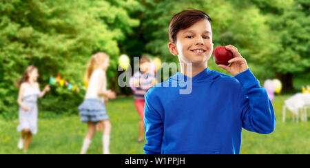 Ragazzo sorridente con mela rossa alla festa di compleanno Foto Stock