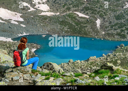 Woman Hiking seduti di fronte lago a forma di cuore lago Chiaretto, Giro di Monviso, Monte Viso, Monviso, Alpi Cozie, Piemonte, Italia Foto Stock