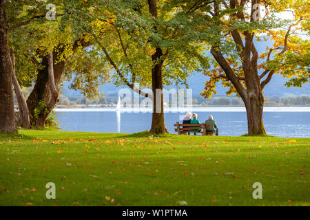 Tre persone anziane seduto sotto grandi alberi su una panchina nel parco e si affacciano sul lago Chiemsee Foto Stock