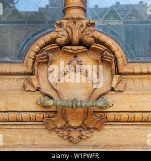 Primo piano del legno e motivo floreale incisioni e manubrio su vecchi battente di porta Foto Stock