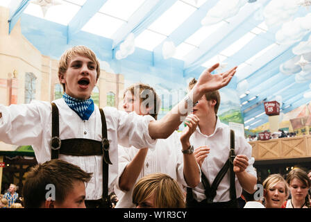 Giovani uomini in pantaloni di pelle in piedi sui banchi di birra Oktoberfest celebrare nella tenda della birra Foto Stock