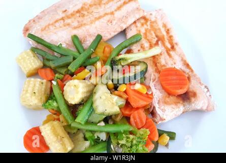 Filetto di salmone con un trito di mais, carote, fagioli verdi, zucchine, pepe e broccoli su una piastra bianca.Verdure miste con frutti di mare. Colorato Pranzo. Foto Stock