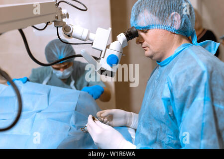 Oculista chirurgo guardando attraverso il microscopio chirurgico facendo operazione difficoltosa. Foto Stock