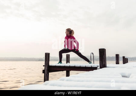 Giovane donna stretching su un molo sul Lago di Starnberg, Baviera, Germania. Foto Stock