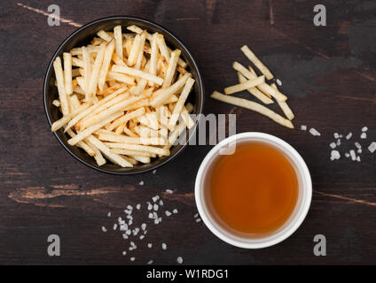 Sale e aceto bastoncini di patate in bianco ciotola, classico snack con ketchup sul legno. Foto Stock