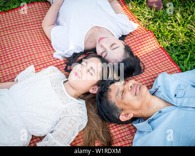 Le famiglie asiatiche rilassarsi nel parco durante l'estate. La famiglia in un parco, papà, mamma e figlia si sono addormentati sull'erba. Foto Stock