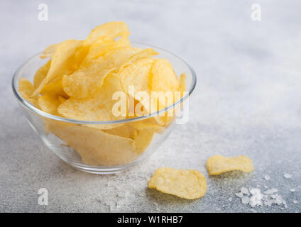 Ciotola di vetro piatto con patatine chips con aroma di cipolla con sale su sfondo chiaro. Foto Stock