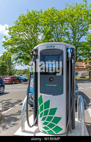 Punto di ricarica per i veicoli elettrici situati in un parcheggio. Le sue credenziali ecologiche sono sottolineati dal verde delle foglie di un albero contro cui è s Foto Stock