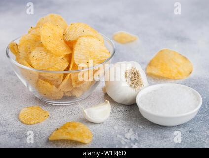 Ciotola di vetro piatto con patatine chips con aglio e sale su sfondo chiaro. Foto Stock