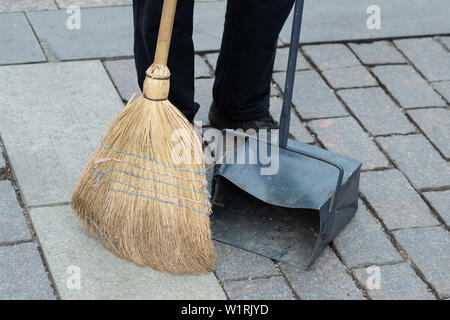 Descrizione: lavoratore comunale spazzare la strada con manico e raccoglie la spazzatura in scoop. igiene lavoratore sweep street Foto Stock