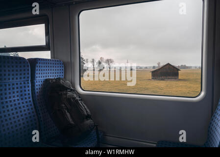 Treno tedesco interno con uno zaino nero sulla sedia blu e una casetta di legno visualizzati sulla finestra del treno. Autunno del concetto di viaggio. Foto Stock