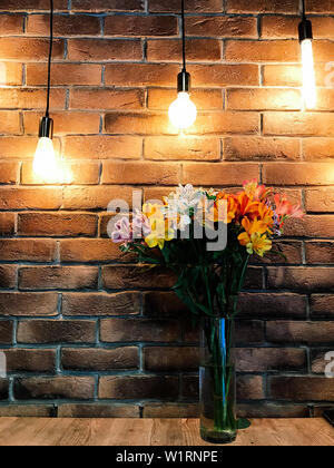 Un bouquet di fiori colorati di Alstroemeria sullo sfondo di un muro di mattoni in interni con luce artificiale. Un bouquet di coloratissimi fiori di primavera di Foto Stock