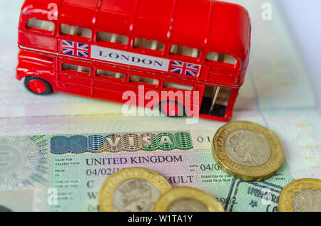 Regno Unito vignetta visto in un passaporto circondato da cancelletto monete e double-decker bus modello. Concetto per i viaggi e le vacanze. Foto Stock