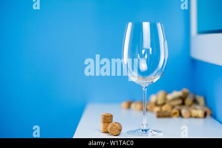 Un vuoto di vetro del vino su uno sfondo blu sorge su un tavolo bianco. I tappi di sughero da bottiglie di vino. Degustazione di vini costosi. Foto Stock