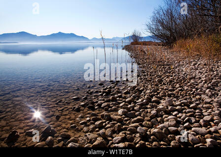 Fondale basso accanto a una banca di ghiaia nel lago Chiemsee e le montagne di Chiemgau in background Foto Stock