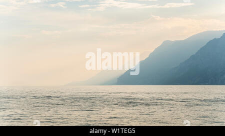 In piedi presso il lago di Garda in Italia e si affaccia l'acqua verso le montagne Foto Stock
