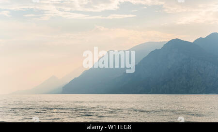 In piedi presso il lago di Garda in Italia e si affaccia l'acqua verso le montagne Foto Stock