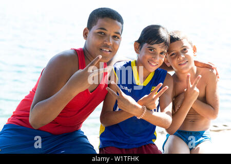 Tre giovani ragazzi locali lungo la riva, segno di vittoria, Cienfuegos, Cuba, isola dei Caraibi Foto Stock